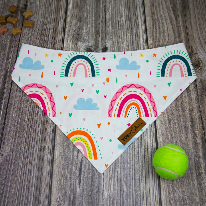 Colorful rainbow-patterned bandana on a wooden surface with a tennis ball.