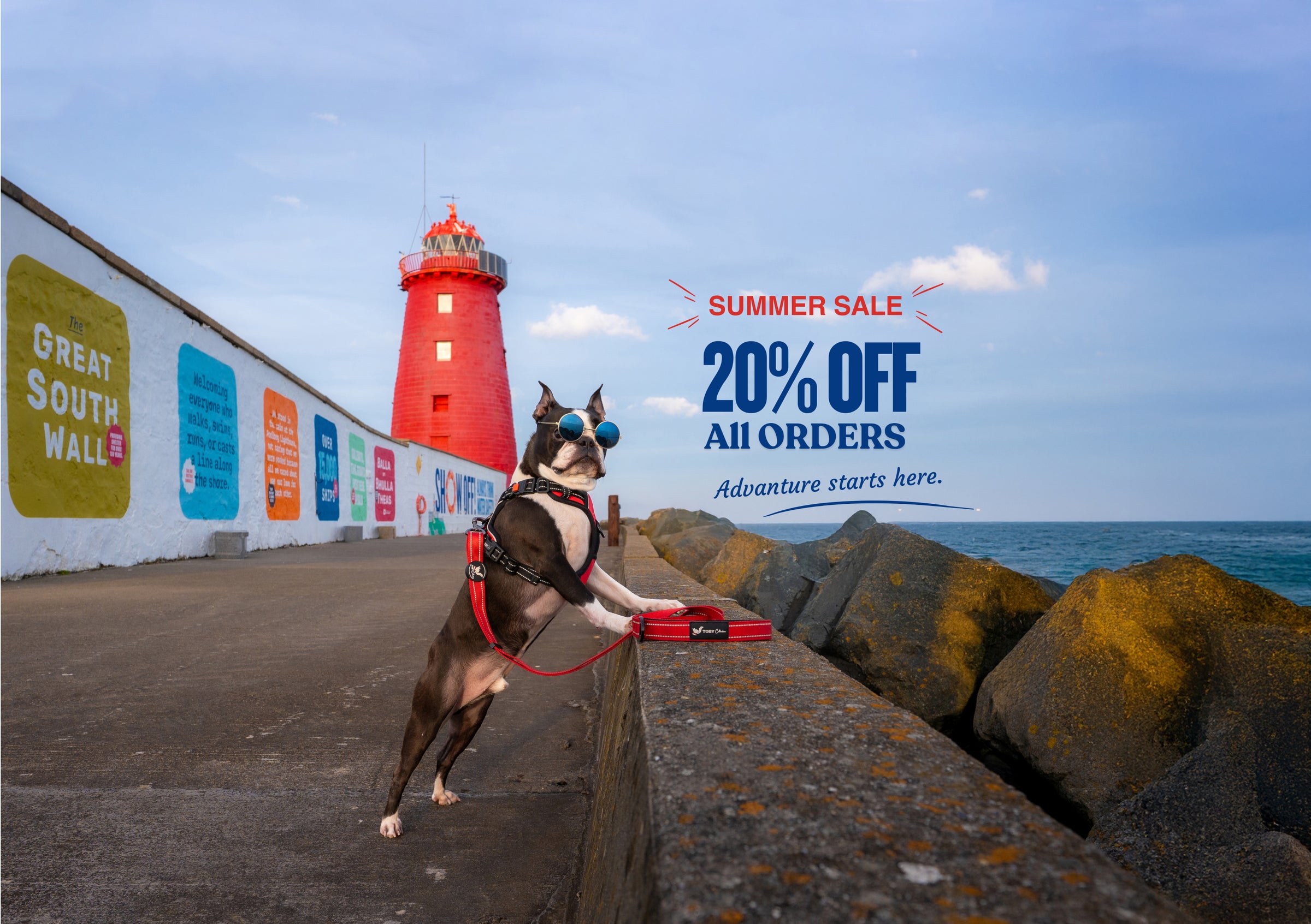 Dog on a leash near a red lighthouse with a summer sale advertisement in the background.