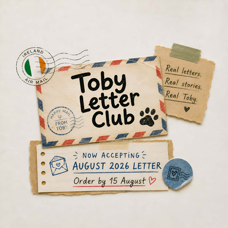 A styled flat-lay of vintage-style letter stationery on a warm off-white background. The main item is a cream-colored envelope with red and blue striped border and the text 'Toby Letter Club' in black, alongside a black paw print and a blue 'Happy Mail FROM TOBY' stamp.