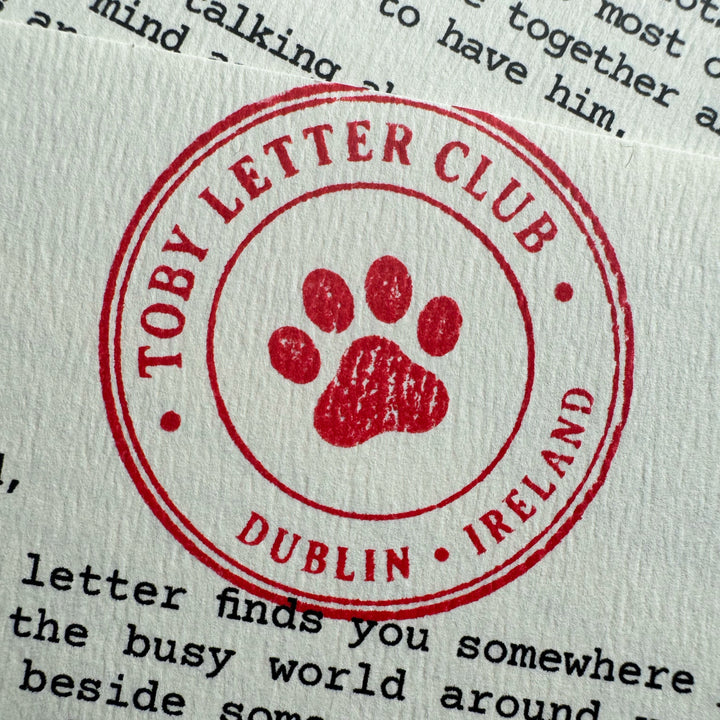 A red circular stamp reading 'TOBY LETTER CLUB' and 'DUBLIN IRELAND' with a paw print in the center, stamped over printed text on white paper.