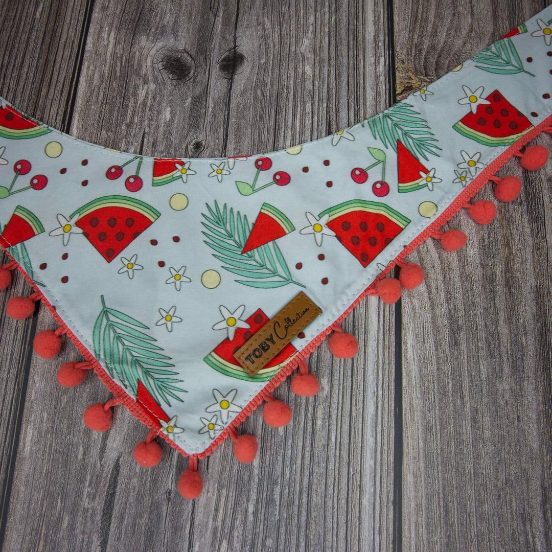 Fabric strip with watermelon pattern and pom-pom trim on a wooden surface