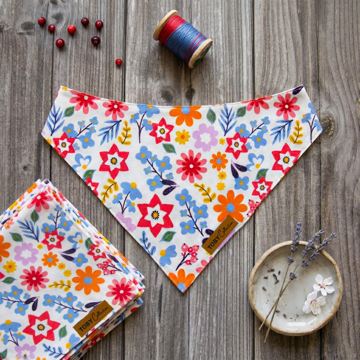 Floral patterned bandanas on a wooden surface with thread and a small dish.
