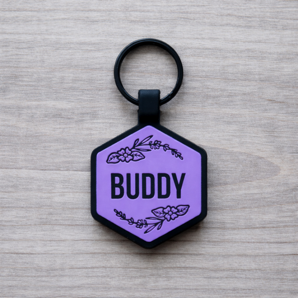 Hexagonal purple pet tag with 'Buddy' and floral designs on a wooden surface