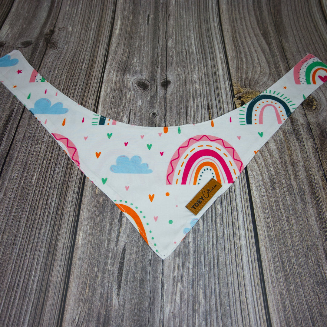 Toby Collection Rainbow Dreams dog bandana on a rustic wooden base.