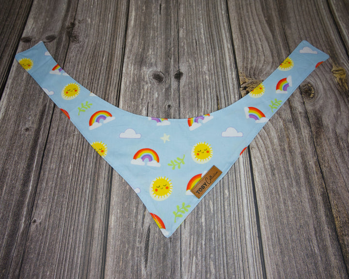 Toby Collection rainbow print dog bandana on a rustic wooden base.