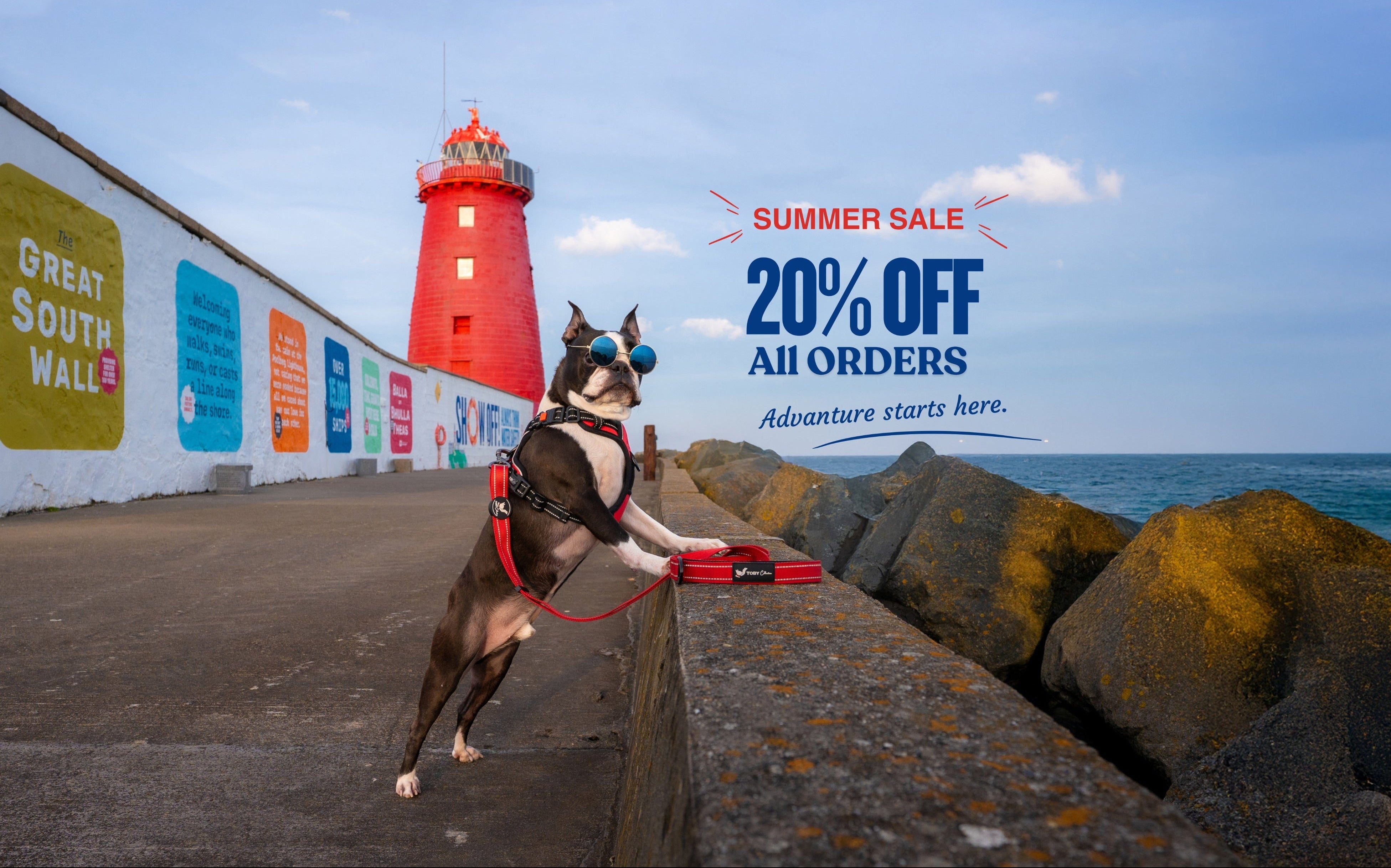 Dog on a leash near a red lighthouse with a summer sale advertisement in the background.